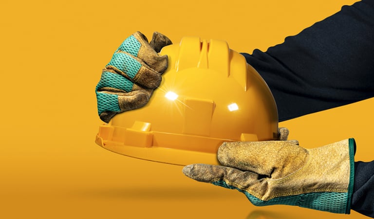 Mãos com luvas protetoras de trabalho segurando um capacete de segurança amarelo