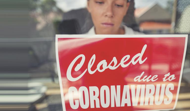 Store owner putting up a closed sign in the window. Sign says: closed due to coronavirus