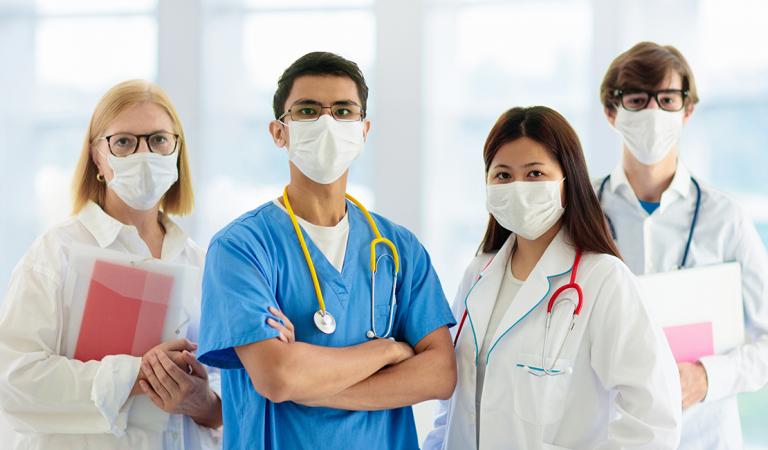 Mixed race Asian and Caucasian doctor and nurse meeting. Clinic personnel wearing face mask and stethoscope.