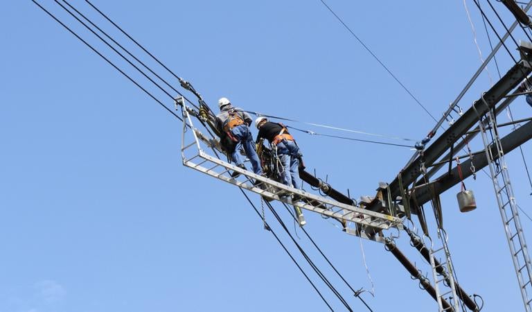 Two electricians working high above on a electricity pylon. Photo: iStockphoto