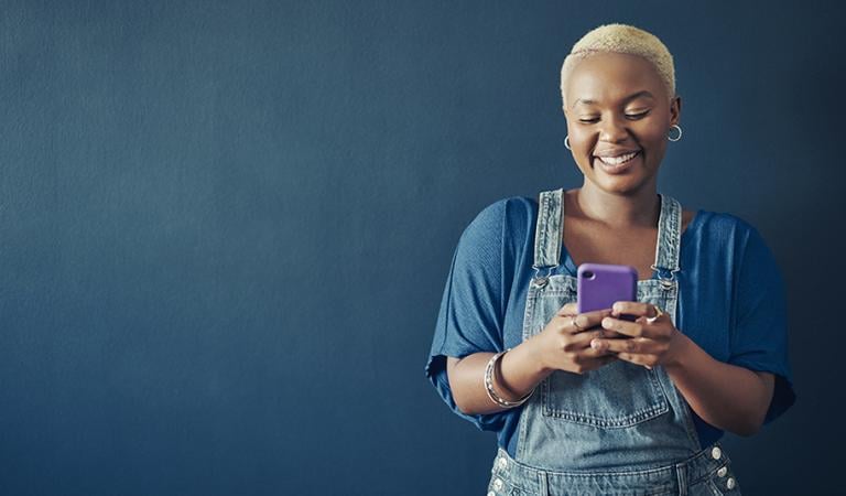 Donna sorridente in tuta che manda un sms sul suo telefono su uno sfondo blu
