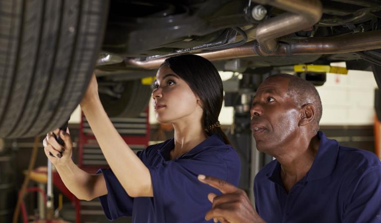 Mechanic and female trainee working underneath car together